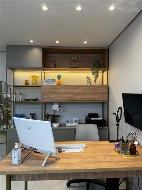 Mesa do consultório com computador e estante iluminada ao fundo